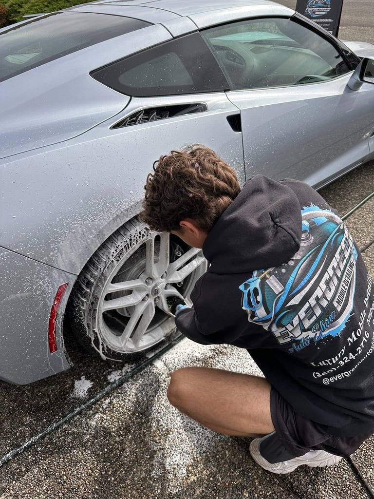 Detailer crouching to wash the wheel of a silver sports car with thick white foam