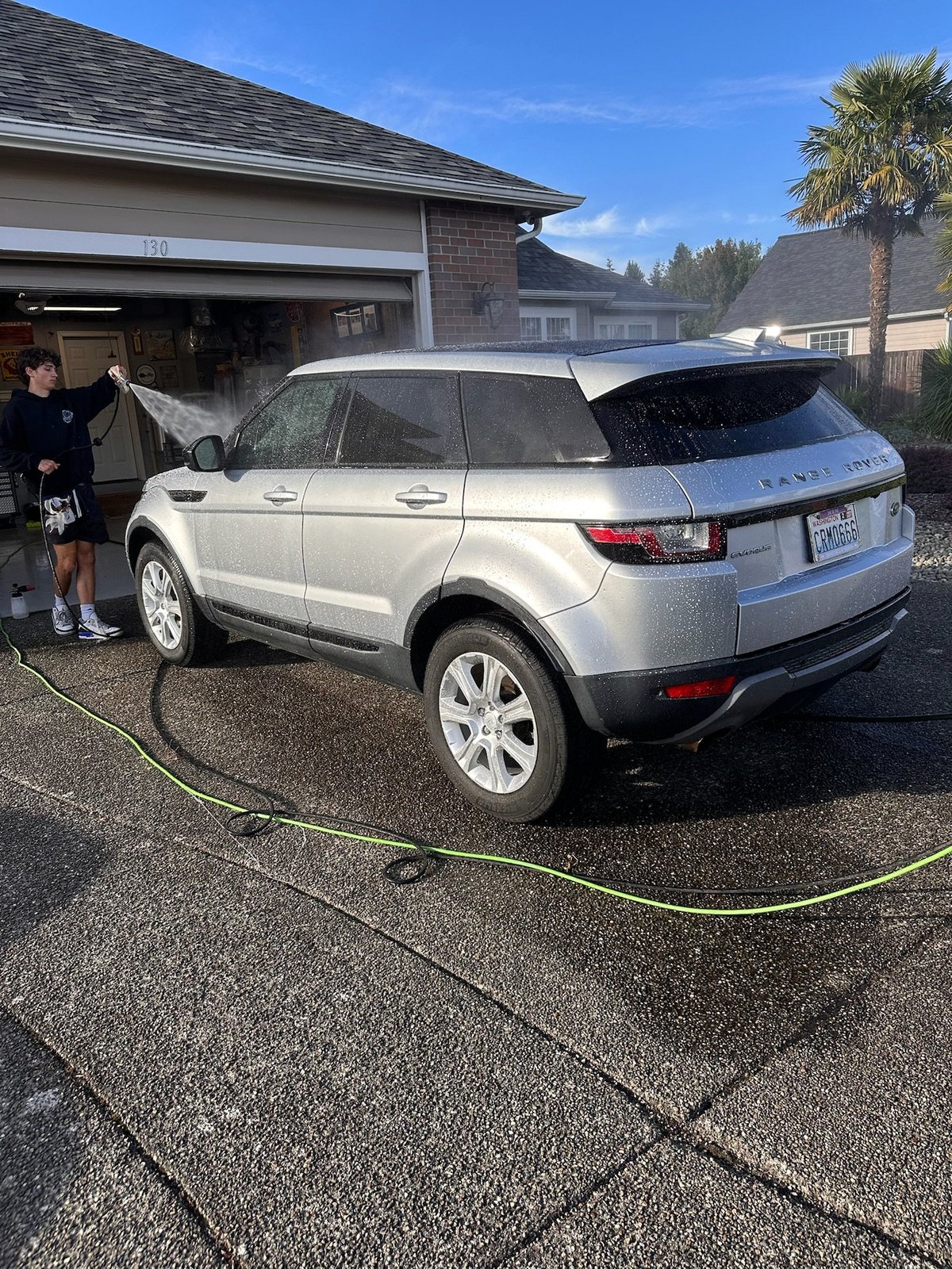 White Range Rover Evoque being charged in a residential driveway with a person standing nearby after detailing