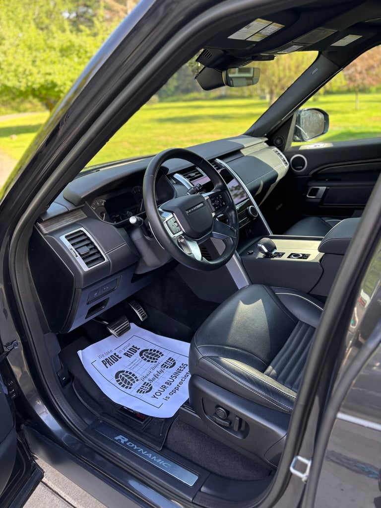 Interior view of a luxury SUV with steering wheel, dashboard, and green landscape visible through open driver door