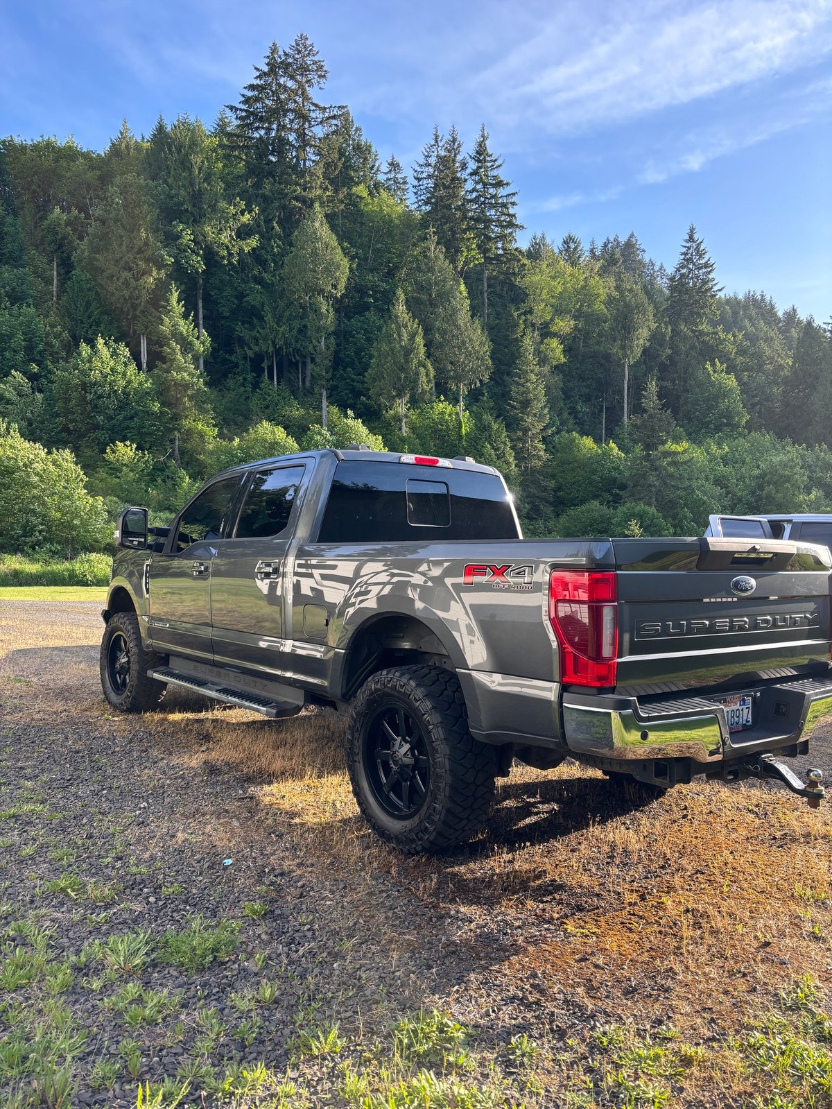 Silver lifted Ford pickup truck parked on gravel with a forested background on a sunny day