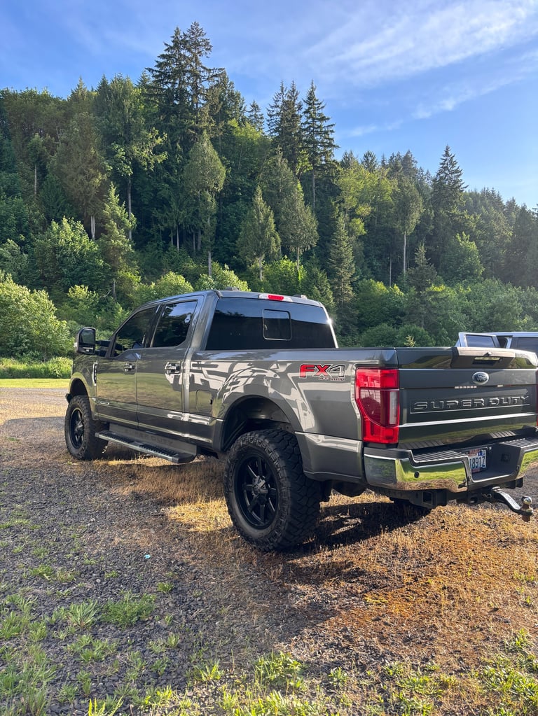 Silver lifted Ford pickup truck parked on gravel with forested background on sunny day