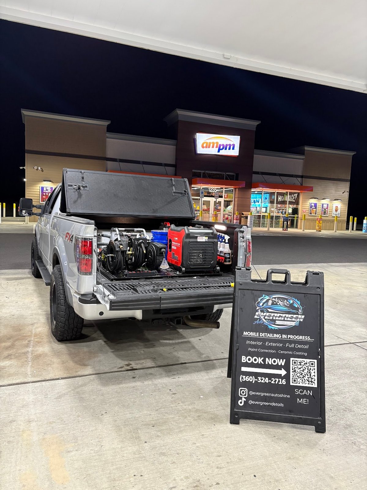 White pickup truck with open tailgate displaying tools and detailing equipment in a parking lot, with an A-frame sign promoting Evergreen Autoshine services in the foreground